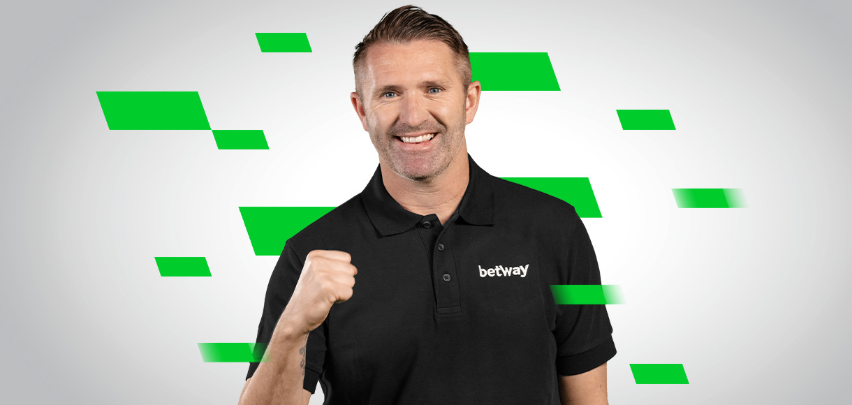 Homme en polo noir avec le logo « betway », souriant et levant le poing sur un fond blanc avec des formes géométriques vertes.