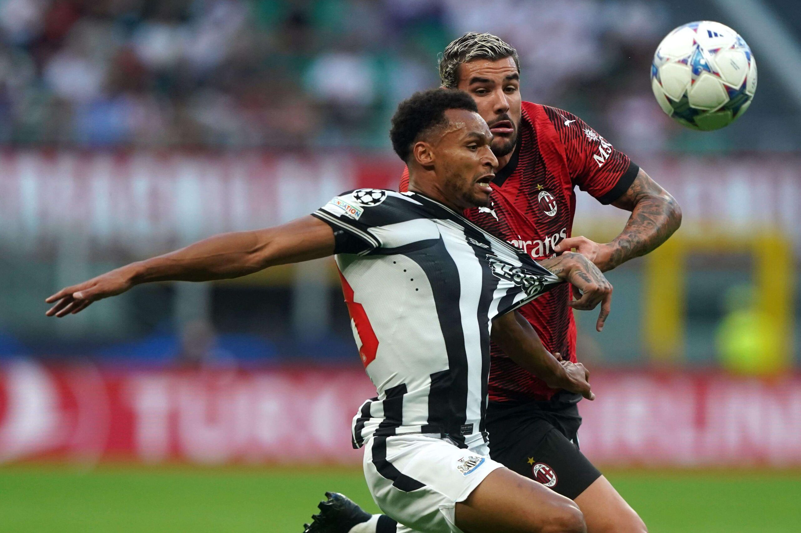 Two soccer players, one in a black and white striped jersey and the other in red and black, are in action during a Betway-sponsored match. The player in stripes kicks the ball aggressively as the other closely marks him, with the blurred crowd providing an electric atmosphere.