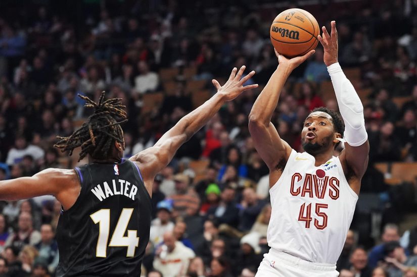 A basketball player in a white Cavs jersey, number 45, leaps for a shot as number 14 in black attempts to block him. The electrifying action unfolds amidst the blurred cheers of an indoor stadium crowd, reminiscent of a thrilling Betway Arabia sporting event.