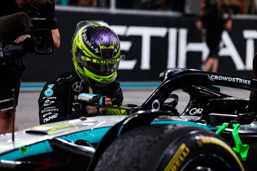 A race car driver wearing a helmet sits in a Mercedes-AMG Formula 1 car as the Betway logo gleams prominently. Nearby, a cameraman captures every moment while the driver performs precise checks on the steering wheel. The scene unfolds against the backdrop of a racetrack.