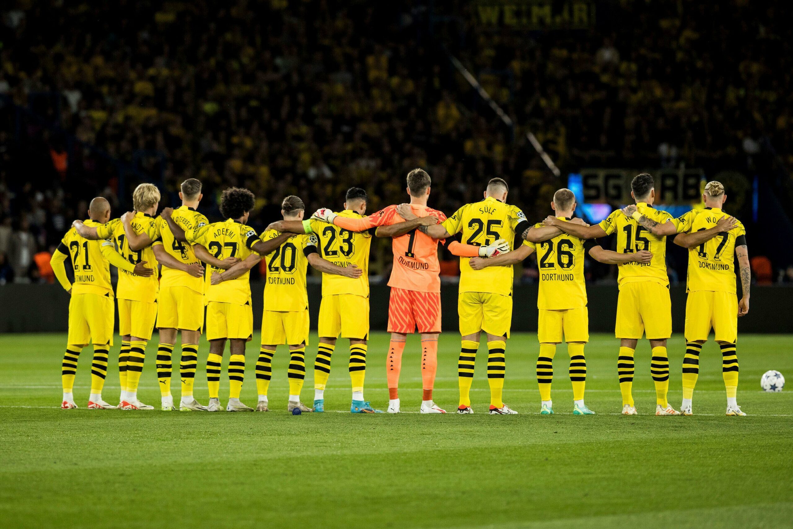 A soccer team in yellow and black uniforms stands in a line with arms linked before a match on a green field, embodying unity and focus as if setting the stage for an exhilarating game. Sponsored by Betway, they are poised to dazzle their fans with skillful play and teamwork.