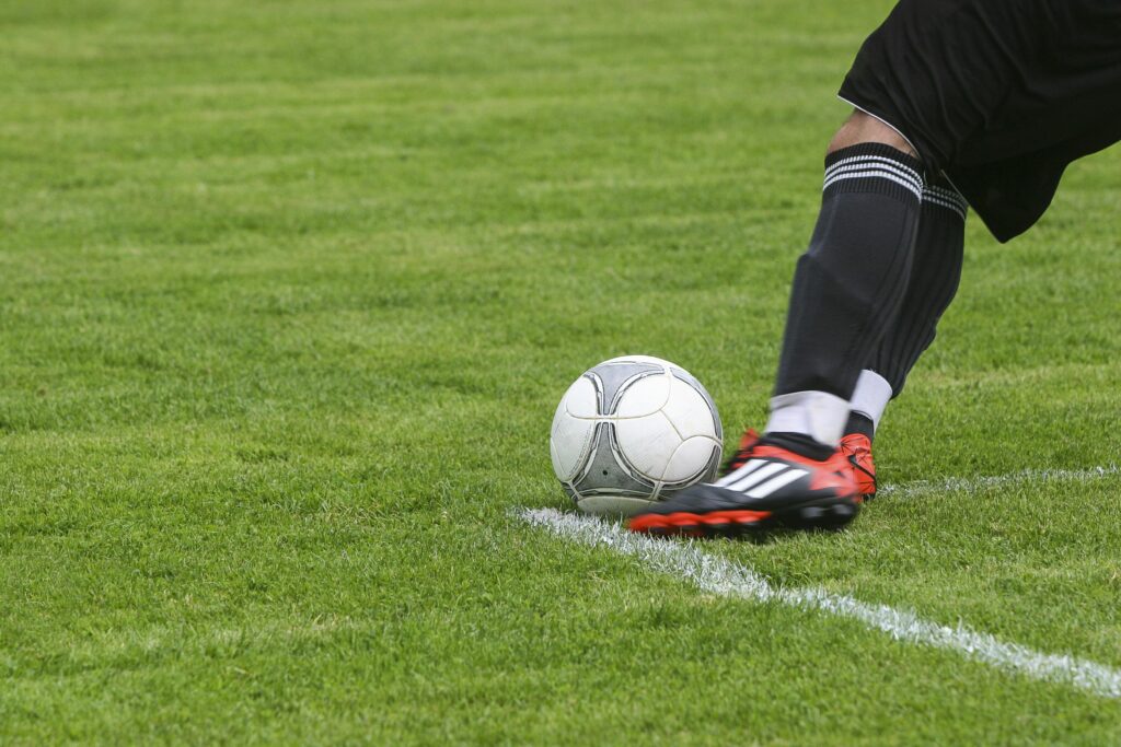 A soccer player in black socks and red cleats, sponsored by Betway, prepares to kick a white soccer ball on a grassy field.