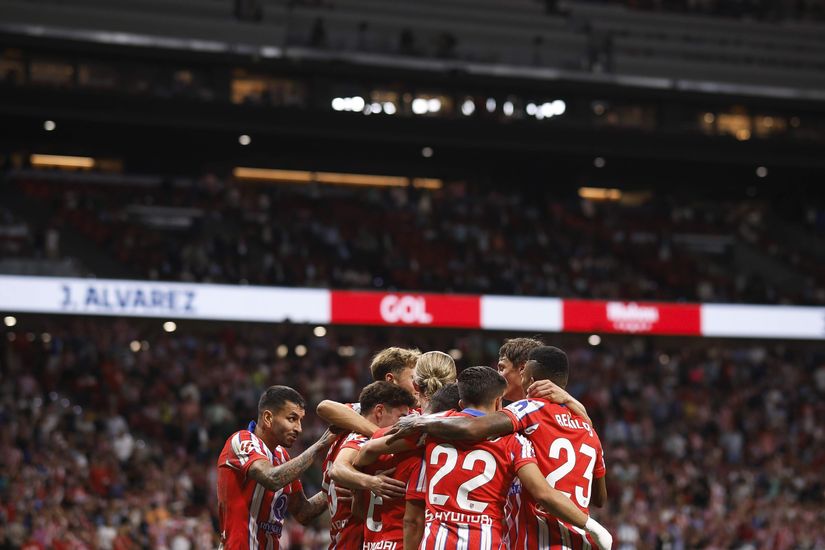 The soccer team in red and white jerseys celebrates a goal by huddling together on the field, with a blurred audience in the background, embodying the vibrant spirit of Betway Arabia.