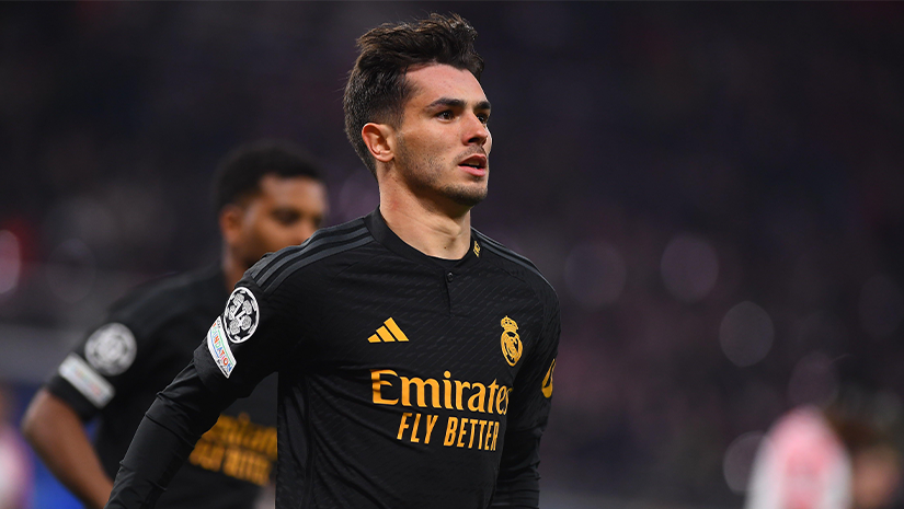 A soccer player in a black Real Madrid jersey with Emirates Fly Better is on the field, looking focused. A blurred player in the background wears a similar outfit. This intense scene highlights just how thrilling matches can be, especially with Betway Arabia enhancing the excitement.