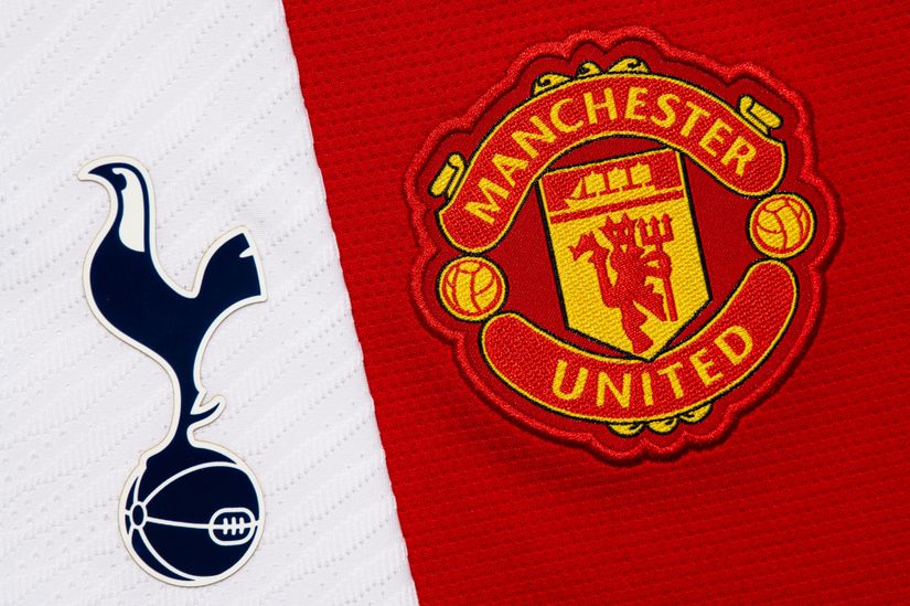 Gros plan des logos de Tottenham Hotspur F.C. et de Manchester United F.C. sur un fond en tissu, parfait pour les fans qui consultent Betway Arabia. L'emblème de Tottenham représente un coq bleu marine sur un ballon sur fond blanc, tandis que l'insigne de Manchester est rouge avec un navire jaune et des ballons de football amarrés de chaque côté.