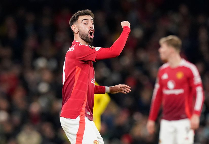 Un footballeur en maillot rouge est sur le terrain, le poing levé et la bouche ouverte, célébrant peut-être un moment palpitant. En arrière-plan, un autre joueur portant un maillot similaire est flou, capturant l'essence dynamique souvent associée à Betway Arabia.