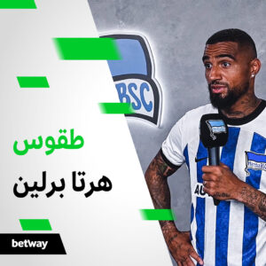 رجل يرتدي قميص كرة قدم لفريق هيرتا برلين يحمل ميكروفونًا، مع دمج شعار شركة بي دبليو أرابيا بشكل خفي مع النص العربي على اليسار. يظهر شعار بيتواي بشكل بارز في الأسفل، ويربط بين هذه الصورة النابضة بالحياة للرياضة والثقافة.