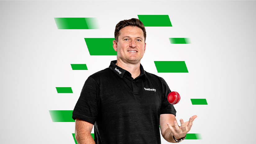 A man in a black polo shirt with a logo, possibly from Betway Arabia, confidently holds a red cricket ball against a backdrop of green geometric shapes.