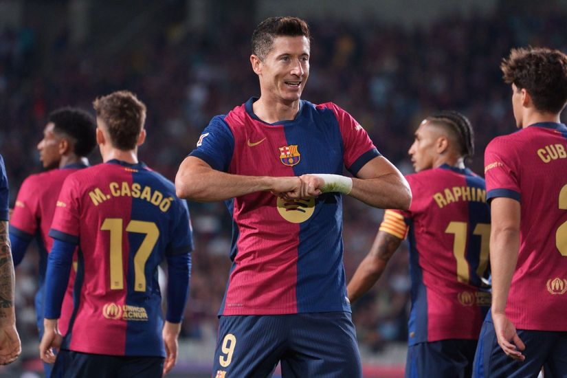 Soccer player in red and blue uniform celebrates on the field among teammates during a match, as the excitement of Betway Arabia sponsorship electrifies the stadium.