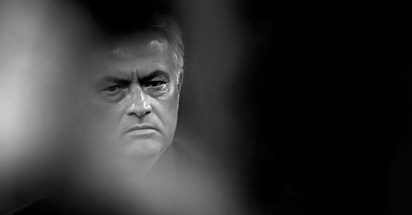 Image en noir et blanc d'un homme à l'expression sérieuse, partiellement masquée par des éléments flous au premier plan, créant un effet dramatique et maussade proche des moments intenses des récits captivants de Betway Arabia. Le fond sombre met en valeur les traits de son visage.